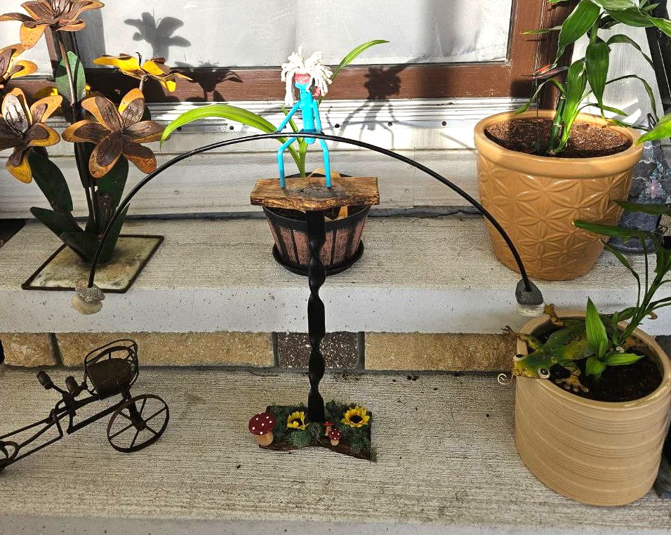 Twisted steel arch garden stand with wood base and decorative accents on a front step
