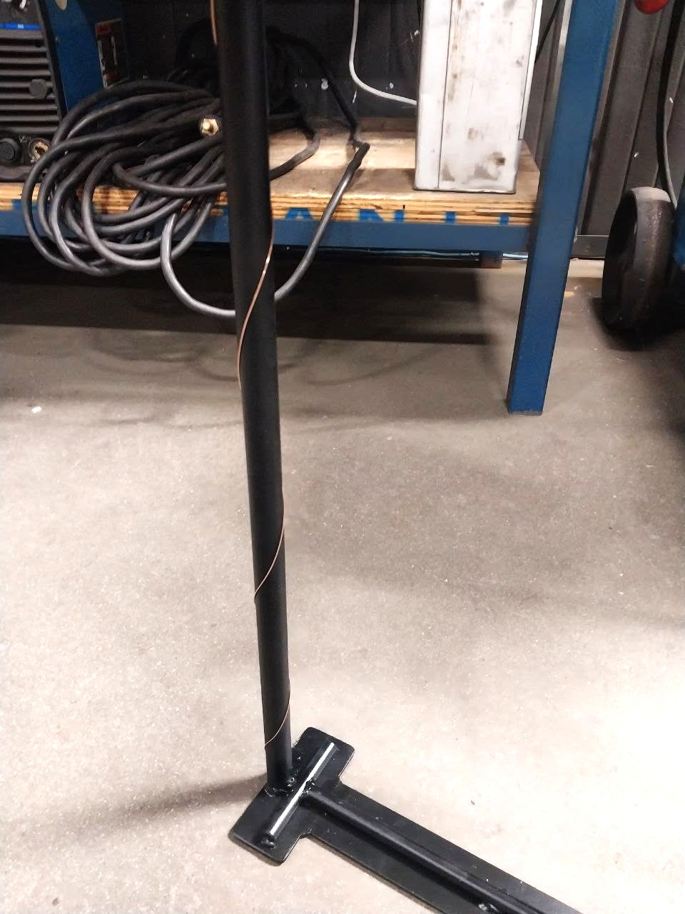 Black powder-coated steel pole with copper accent stripe on a welded T-base