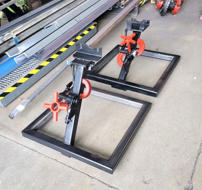 Pair of black powder-coated rolling repair stands with geared rotating heads