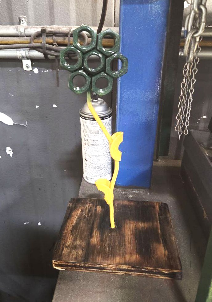 Decorative flower sculpture welded from hex nuts and steel scrap on a torched wood base