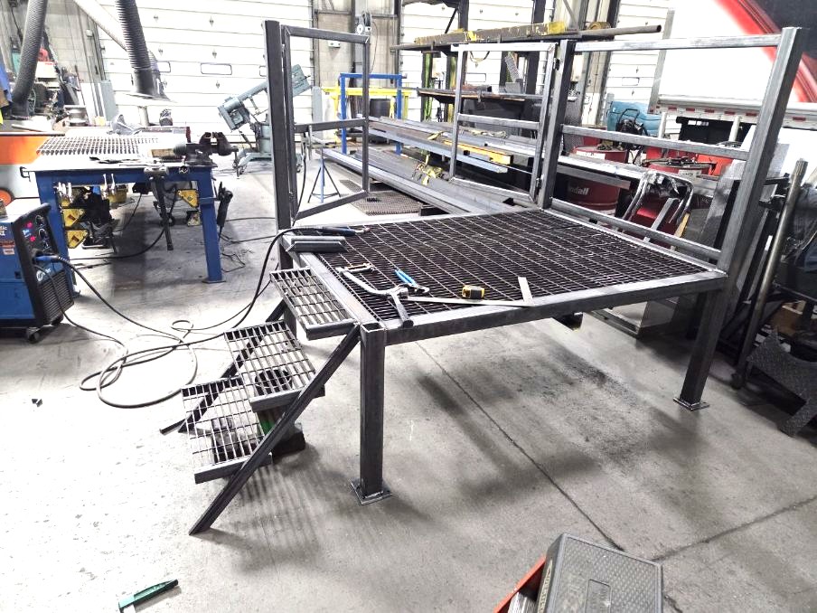 Bare steel work platform with grated decking and stair stringers, in progress on the shop floor