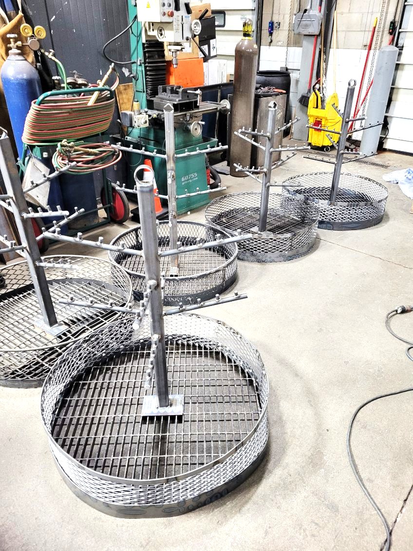 Batch of custom fabricated round fire pit grill grates with center posts and expanded metal baskets