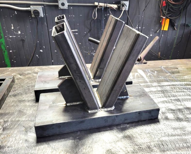 Welded steel display sample showing tube, angle, and flat bar joints on a heavy base plate