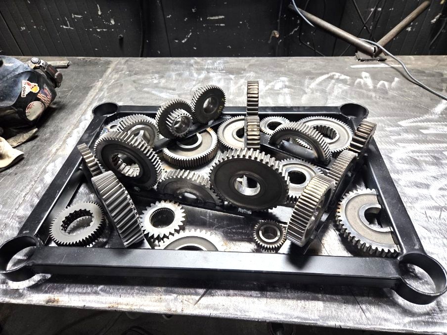 Steel wrench-frame art piece laid out with transmission gears before final welding