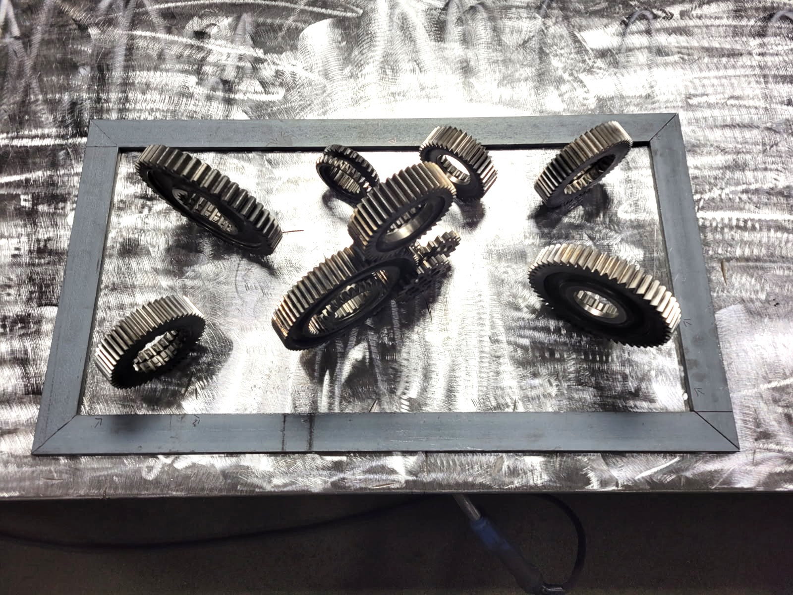 Transmission gears laid out inside a steel frame for a custom industrial gear art piece